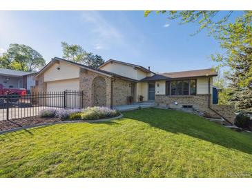 Charming home featuring manicured lawn, brick accents, black fence, and attached two-car garage at 10909 W 65Th Way, Arvada, CO 80004