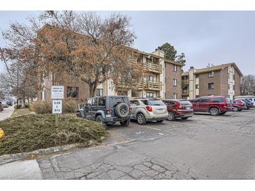 A view of a brick condominium building with a parking lot in front of it on a cloudy day at 1358 S Irving St # 53, Denver, CO 80219