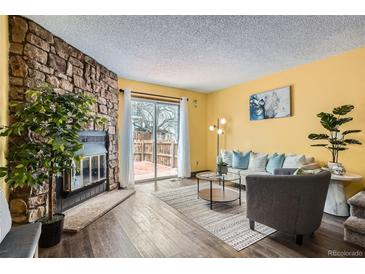 Bright living room featuring a stone fireplace, wood floors, and sliding door access to the outdoor area at 15566 E Louisiana Ave, Aurora, CO 80017