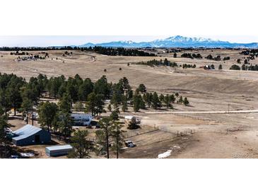 Expansive property featuring rolling hills, mature trees, and a charming farmhouse against a backdrop of snow-capped mountains at 1991 County Road 132, Elizabeth, CO 80107