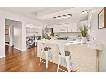 Bright kitchen boasts white cabinets, a stylish island with bar stools, stainless steel appliances, and adjacent laundry area at 1827 Quail St # 8, Lakewood, CO 80215