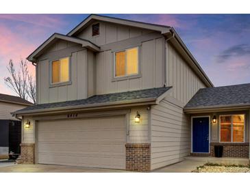 Two-story home featuring a beige exterior, attached garage, blue front door, and well-maintained landscaping at 6414 Stuart St, Arvada, CO 80003