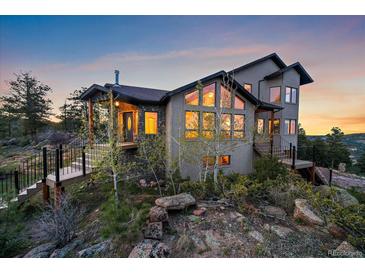 Stunning exterior view of a multi-story home, complemented by mature trees and natural rock outcroppings at 23007 Big Game Trl, Conifer, CO 80433