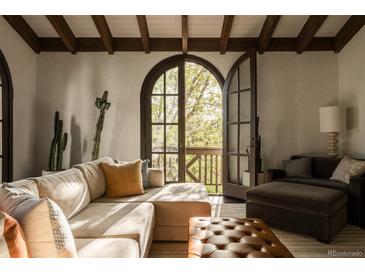 Inviting living room featuring exposed beam ceiling, comfortable seating, and natural light from the arched window at 3 Carriage Brook Rd, Cherry Hills Village, CO 80121
