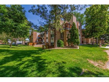 Brick apartment building nestled in lush green landscape with mature trees providing ample shade on a bright sunny day at 6455 E Bates Ave # 4-105, Denver, CO 80222
