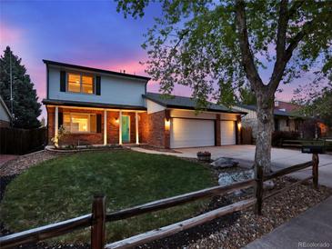 Charming two-story home with a well-manicured lawn, brick accents, and a three-car garage at dusk at 13935 E Idaho Pl, Aurora, CO 80012