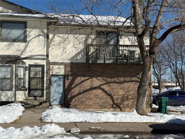 Two-story townhome with brick accents, a walkout patio, and snowy ground at 1868 S Ammons St # D, Lakewood, CO 80232