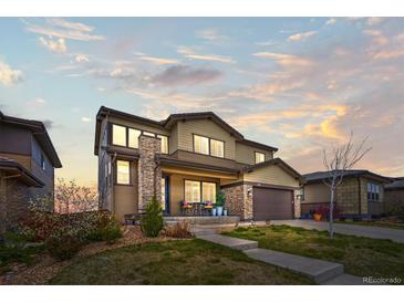 Two-story home featuring a manicured lawn, stone accents, and a covered front porch with seating at 14102 Night Owl Ln, Parker, CO 80134