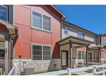Modern townhome featuring a red exterior, stone accents, and a charming white picket fence at 1353 Reynolds St # 2B, Fort Lupton, CO 80621
