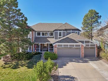 Stunning two-story home featuring a three-car garage, manicured lawn, mature trees and welcoming front porch at 9977 Falcon Creek Dr, Highlands Ranch, CO 80130