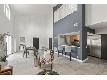 Open-concept living room with high ceilings, sleek gray tile floors, and a modern eat-in kitchen bar with stainless steel appliances at 837 E 17Th Ave # 2K, Denver, CO 80218