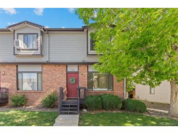 Charming townhouse with brick facade, red door, green wreath, and lovely front yard landscaping at 10693 W 63Rd Dr # 106, Arvada, CO 80004