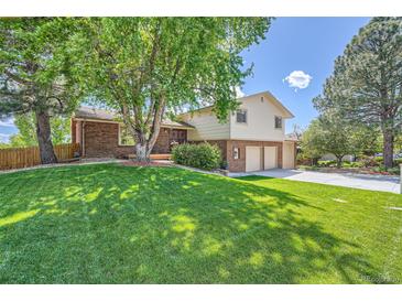 Landscaped front yard featuring a lush green lawn, mature trees, and charming two-story brick accents at 11410 W 72Nd Pl, Arvada, CO 80005