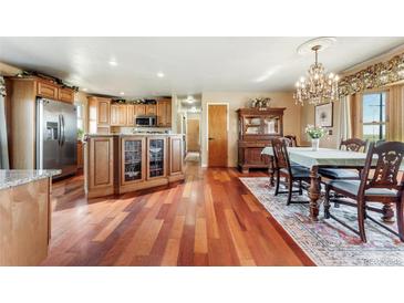 Open kitchen with an island with wood cabinets and hardwood floors into the dining room with chandelier lighting at 4295 S County Road 193, Byers, CO 80103