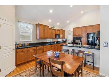 Well-lit kitchen featuring wood cabinetry, granite counters, and a cozy breakfast bar with seating at 6679 S Robb St, Littleton, CO 80127