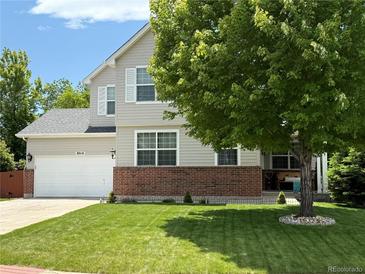 Charming two-story home features a well-manicured lawn, brick accents, light gray siding, and a classic white two car garage door at 8010 Raspberry Dr, Frederick, CO 80504