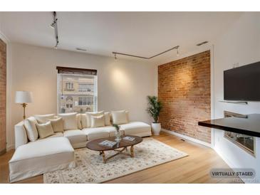 Cozy living room featuring a large sectional sofa, wood floors, exposed brick, and ample natural light at 2306 Glenarm Pl # 206, Denver, CO 80205