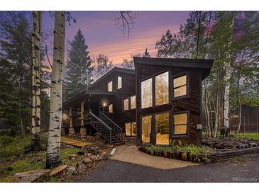 Modern exterior featuring wood paneling, large windows, and a picturesque natural setting with stunning sunset colors at 10419 Christopher Dr, Conifer, CO 80433