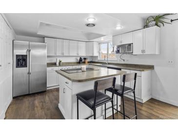 Updated kitchen with white cabinets, island with bar seating, stainless steel appliances, and wood floors at 9044 E Nassau Ave, Denver, CO 80237