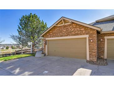Attached two-car garage with stone facade and concrete driveway, next to a tree and a view at 7511 S Sicily Way, Aurora, CO 80016