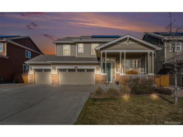 Inviting two-story home featuring a three-car garage, covered porch, stone accents, and solar panels on the roof at 6021 Lynx Creek Cir, Erie, CO 80516