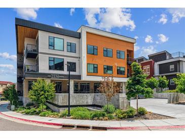 Modern condo building with orange and gray exterior, landscaped grounds, and visible signage, under a partly cloudy sky at 2876 W 53Rd Ave # 305, Denver, CO 80221