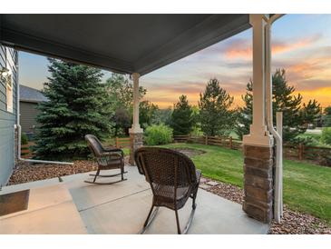 Covered patio features stone pillars, rocking chairs and views of the landscaped yard and sunset at 19067 W 57Th Dr, Golden, CO 80403