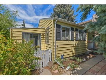 Charming yellow home featuring a white picket fence, siding, and black shuttered windows, nestled under a bright blue sky at 1665 S Madison St, Denver, CO 80210