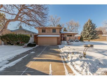 Inviting two-story house featuring a well-kept lawn, mature trees, and a paved driveway in a snow-covered landscape at 7318 W Cedar Cir, Lakewood, CO 80226