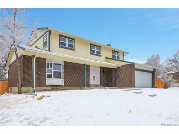 Inviting two-story brick home featuring a covered entryway and attached two-car garage, with a snow-covered front yard at 8694 E Eastman Ave, Denver, CO 80231