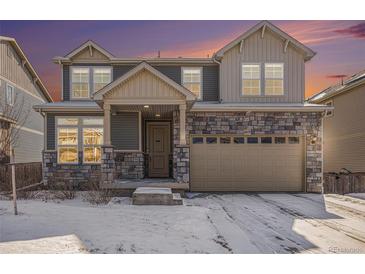 Two-story home with stone accents, an attached two-car garage, and snow-covered front yard at dusk at 16278 E 111Th Pl, Commerce City, CO 80022