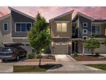 Modern townhome featuring stone accents, a single-car garage, and a manicured front yard with a young tree at 9719 Albion Ln, Thornton, CO 80229