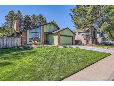 Charming green home featuring brick accents, large windows, manicured lawn and mature trees at 8820 W 80Th Dr, Arvada, CO 80005