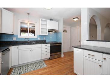 Bright kitchen with white cabinets, stainless steel appliances, blue backsplash, granite counters and hardwood floors at 945 Waite Dr, Boulder, CO 80303