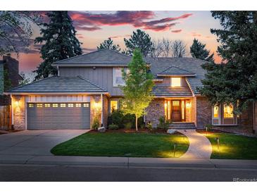 Charming two-story home featuring a brick facade, manicured lawn, and inviting walkway with landscape lighting at dusk at 10849 E Crestridge Cir, Englewood, CO 80111