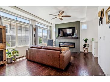 Cozy living room with fireplace, large windows, ceiling fan, and dark wood floors at 10560 Waco St, Commerce City, CO 80022