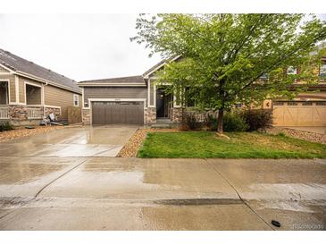 Charming home featuring a two-car garage, stone accents and well maintained landscaping on a wet, overcast day at 12652 Glencoe St, Thornton, CO 80241