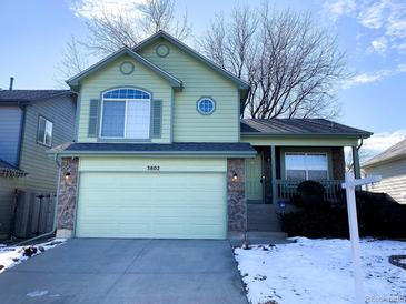 Two-story light green house with a two-car garage and snowy front yard at 3802 Desert Willow Ave, Broomfield, CO 80020