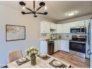 Bright kitchen features white cabinetry, stainless steel appliances, and marble countertops, complemented by a modern chandelier at 3184 S Heather Gardens Way # 302, Aurora, CO 80014