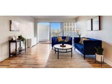 Inviting living room featuring hardwood floors, two blue sofas, modern artwork and sliding glass doors to a balcony at 888 N Logan St # 5A, Denver, CO 80203