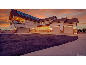 Expansive home featuring a three-car garage, stone accents, and a cozy porch, all under a vibrant sunset sky at 1012 S Addison Way, Aurora, CO 80018