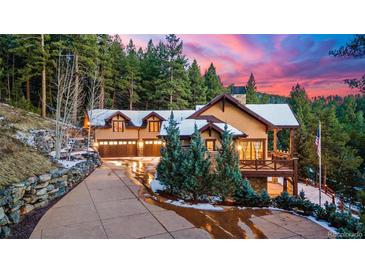 A grand exterior view of a luxury mountain home featuring an attached garage, beautiful landscaping, and stunning sunset at 30 W Ranch Trl, Morrison, CO 80465