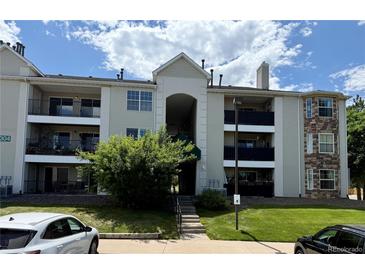 Multi-level condo building with balconies, stone accents, tidy landscaping, and street parking at 12304 W Cross Dr # 304, Littleton, CO 80127