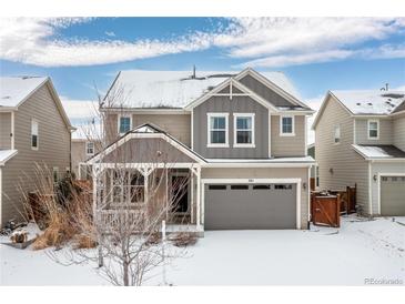 Charming two-story home with a gray garage, a cozy porch, and snow-covered landscape at 381 Rainbow Ln, Lafayette, CO 80026