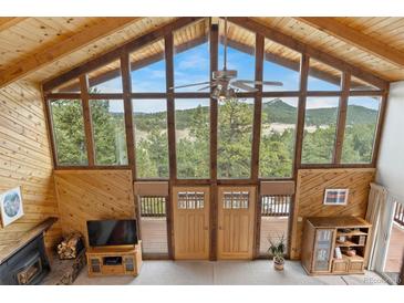 Bright living room featuring wood-paneled walls, vaulted ceilings, a fireplace, and expansive windows with mountain views at 25019 N Mountain Park Dr, Evergreen, CO 80439