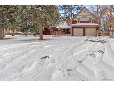 Snow-covered driveway leading to charming red two-story home with attached garage at 7893 Hill Crest Dr, Louviers, CO 80131