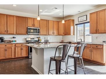 Spacious kitchen features stainless steel appliances, island with barstool seating, and tile backsplash at 5352 Truckee St, Denver, CO 80249