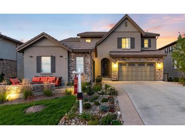 Beautifully landscaped home with stone accents and a cozy front porch seating area, set against a colorful evening sky at 10877 Skydance Dr, Highlands Ranch, CO 80126