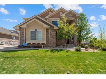 Charming two-story home with stone accents, lush green lawn, and professionally landscaped front yard at 17102 W 85Th Pl, Arvada, CO 80007