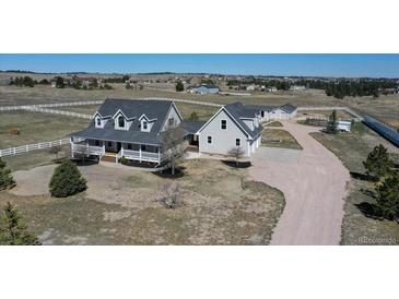 Expansive horse property featuring a light gray home with white trim, a covered porch, paddocks, and stables at 1465 Arabian Trl, Elizabeth, CO 80107